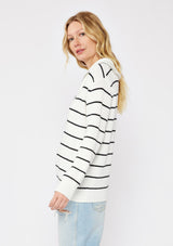 [Color: White/Black] A side facing image of a blonde model wearing a white and black striped knit pullover sweater with a half zip front. 