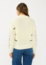 [Color: Cream/Black] A back facing image of a brunette model wearing a cozy striped knit sweater with a cable knit detailing. Featuring a crew neckline and  long sleeves with a dropped shoulder. A cold weather staple for the fall and winter season. 