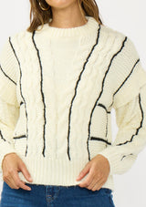 [Color: Cream/Black] A detail image of a brunette model wearing a cozy striped knit sweater with a cable knit detailing. Featuring a crew neckline and  long sleeves with a dropped shoulder. A cold weather staple for the fall and winter season. 
