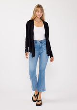 [Color: Black] A front facing image of a blonde model wearing a black solid knit sweater with a wrap front and side button closures. A soft versatile sweater, perfect for spring styling. 