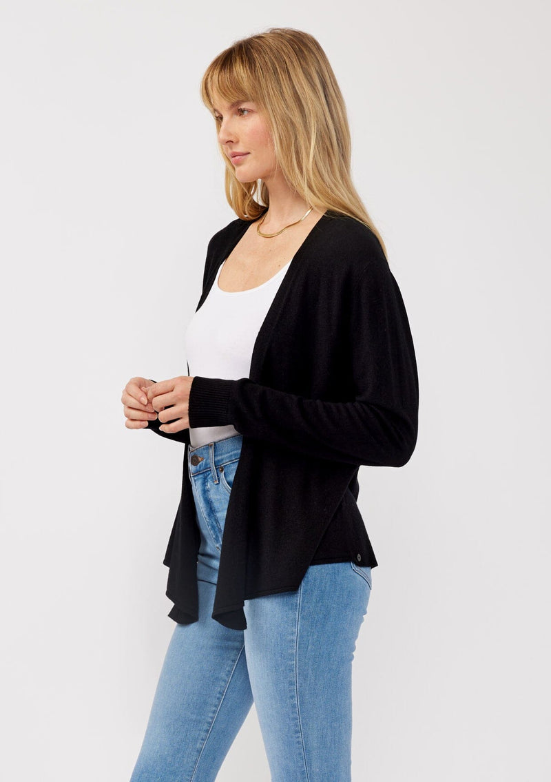 [Color: Black] A side facing image of a blonde model wearing a black solid knit sweater with a wrap front and side button closures. A soft versatile sweater, perfect for spring styling. 