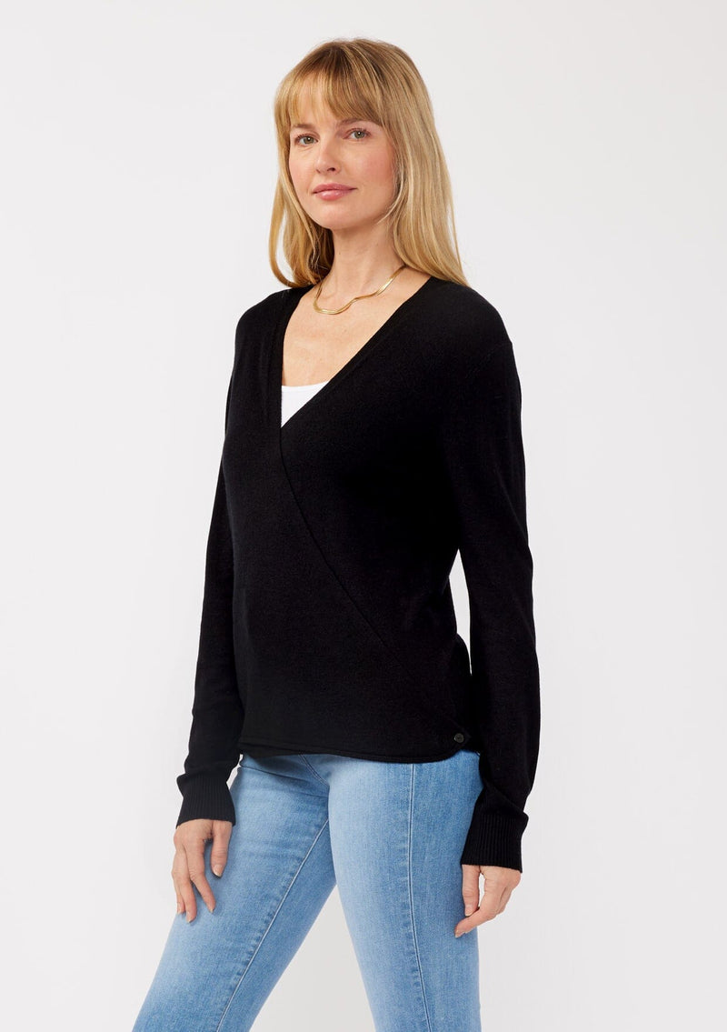[Color: Black] A side facing image of a blonde model wearing a black solid knit sweater with a wrap front and side button closures. A soft versatile sweater, perfect for spring styling. 