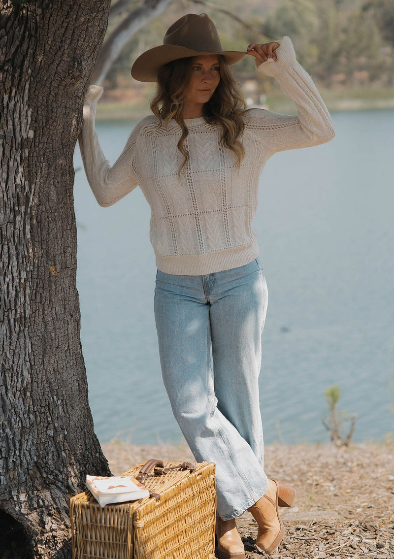 [Color: Blush] A front facing image of a blonde model at the lake wearing a fuzzy open knit pullover sweater with a crew neckline, long sleeves, and a flutter cuff. Lightweight and breezy for the fall season. 