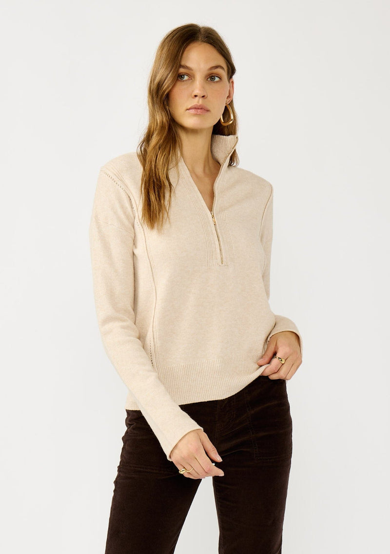 [Color: Dusty Blush] A front facing image of a blonde model wearing a cozy beige turtle neck sweater with a half zip front, long sleeves, and ribbed trims. A basic pullover sweater for the fall season. 