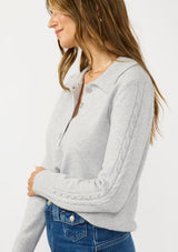 [Color: Heather Silver] A detail image of a brunette model wearing a soft grey polo sweater with a collared neck, button front, and cable knit detail.