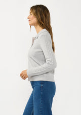 [Color: Heather Silver] A side facing image of a brunette model wearing a soft grey polo sweater with a collared neck, button front, and ribbed trim. 