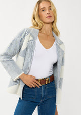 [Color: White/Dusty Blue] A front facing image of a blonde model wearing a blue striped sweater jacket with white geometric accents. Featuring a notched lapel, double-breasted front, snap buttons, and side pockets. A cozy and chic fall sweater for the office and casual outings. 