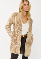 [Color: Sand] A front facing image of a blonde model wearing a brown floral print cardigan with a soft, fuzzy texture featuring an open front and patch pockets. 