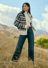 [Color: Cream/Black] A front facing image of a brunette model wearing a black and cream button front knit sweater with a high neckline and side pockets. A bohemian knit sweater for cozy fall styling. 
