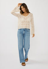 [Color: Natural] A front facing image of a brunette model wearing a beige crochet knit top with long bell sleeves and a v-neckline. A breezy beach top for spring and summer. 