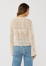 [Color: Natural] A back facing image of a brunette model wearing a beige crochet knit top with long bell sleeves and a v-neckline. A breezy beach top for spring and summer. 