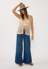 [Color: Natural] A front facing image of a brunette model wearing a beige crochet knit vest with a tie front. Styled with denim for spring.