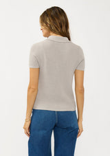 [Color: Light Heather Grey] A back facing image of a brunette model wearing a grey waffle knit polo top with a collared neck and button front. 