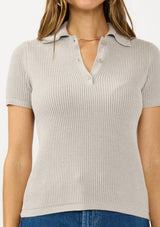 [Color: Light Heather Grey] A detail image of a brunette model wearing a grey waffle knit polo top with a collared neck and button front. 