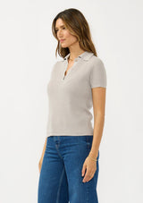 [Color: Light Heather Grey] A side facing image of a brunette model wearing a grey waffle knit polo top with a collared neck and button front. 