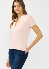 [Color: Light Pink] A side facing image of a brunette model wearing a light pink waffle knit polo top with a collared neck and button front. 