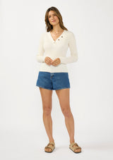[Color: Natural] A front facing image of a brunette model wearing an off white waffle knit sweater top with a v neckline and a button front detail. 