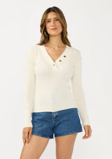 [Color: Natural] A front facing image of a brunette model wearing an off white waffle knit sweater top with a v neckline and a button front detail. 