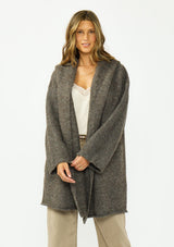 [Color: Dark Heather Brown] A front facing image of a brunette model wearing a brown cozy wool blend coatigan with an oversized fit, hoodie, and side pockets. 