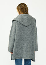 [Color: Heather Charcoal] A back facing image of a brunette model wearing a grey cozy wool blend coatigan with an oversized fit, hoodie, and side pockets. 