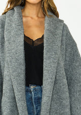 [Color: Heather Charcoal] A detail image of a brunette model wearing a grey cozy wool blend coatigan with an oversized fit, hoodie, and side pockets. 
