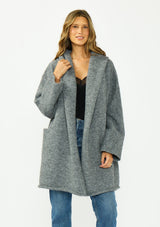 [Color: Heather Charcoal] A front facing image of a brunette model wearing a grey cozy wool blend coatigan with an oversized fit, hoodie, and side pockets. 
