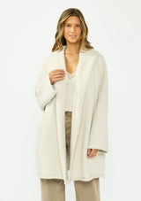 [Color: Heather Cream] A front facing image of a brunette model wearing a cream cozy wool blend coatigan with an oversized fit, hoodie, and side pockets. 