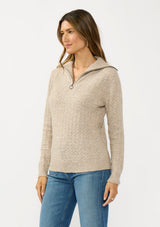 [Color: Heather Cement] A side facing image of a brunette model wearing a brown pointelle knit sweater with a half zip up. 