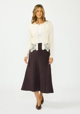 [Color: Bone] A front facing image of a brunette model wearing an ivory lace cardigan with a button front. Paired with  a white top and a brown ribbed skirt. 