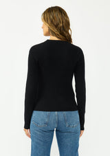 [Color: Black] A back facing image of a brunette model wearing a waffle knit sweater with a crew neckline and a side tie detail. 