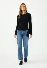[Color: Black] A front facing image of a brunette model wearing a waffle knit sweater with a crew neckline and a side tie detail. 