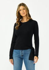 [Color: Black] A front facing image of a brunette model wearing a waffle knit sweater with a crew neckline and a side tie detail. 