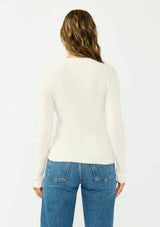 [Color: Natural] A back facing image of a brunette model wearing an off white waffle knit sweater with a crew neckline and a side tie detail. 