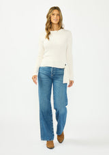 [Color: Natural] A front facing image of a brunette model wearing an off white waffle knit sweater with a crew neckline and a side tie detail. 