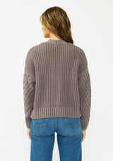 [Color: Mocha] A back facing image of a brunette model wearing a knit cardigan with a button front and v neckline. Paired with dark brown denim. 
