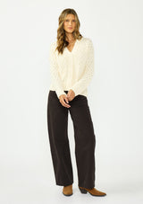 [Color: Natural] A front facing image of a brunette model wearing a cream knit cardigan with a button front and v neckline. Paired with dark brown denim. 
