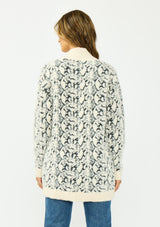 [Color: Cream/Black] A back facing image of a brunette model wearing a snake print cardigan with a fuzzy texture, an open front, and contrast trim. Paired with a lace camisole and a vintage dark wash denim. 