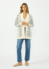 [Color: Cream/Black] A front facing image of a brunette model wearing a snake print cardigan with a fuzzy texture, an open front, and contrast trim. Paired with a lace camisole and a vintage dark wash denim. 
