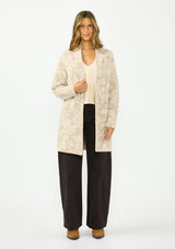 [Color: Taupe] A front facing image of a brunette model wearing a light beige floral cardigan with an open front and patch pockets. Paired with dark brown denim and boots. 