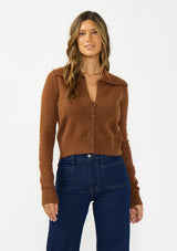 [Color: Brown] A front facing image of a brunette model wearing a brown cropped sweater with a wide collar, button front, and ribbed trim. Styled with a dark was denim. 