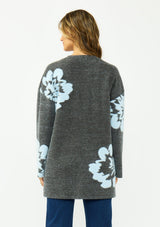 [Color: Charcoal] A back facing image of a brunette woman wearing a dark gray open-front cardigan with large light blue floral patterns on the sleeves and lower front, worn over a white top and blue jeans .