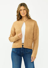 [Color: Camel] A front facing image of a brunette model wearing a camel brown cardigan with an open front, patch pockets, and blanket stitch trims. Styled over a white tee and dark wash denim. 