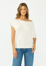 [Color: Natural] A front facing image a brunette model wearing an off white off the shoulder sweater top with short sleeves and a fitted ribbed hem. 