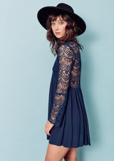 [Color: Dark Navy] A brunette woman wearing a blue sheer lace mini dress. Featuring a feminine v neckline, a button front detail, an empire waist, long sheer lace bell sleeves, and a sexy sheer lace back detail.