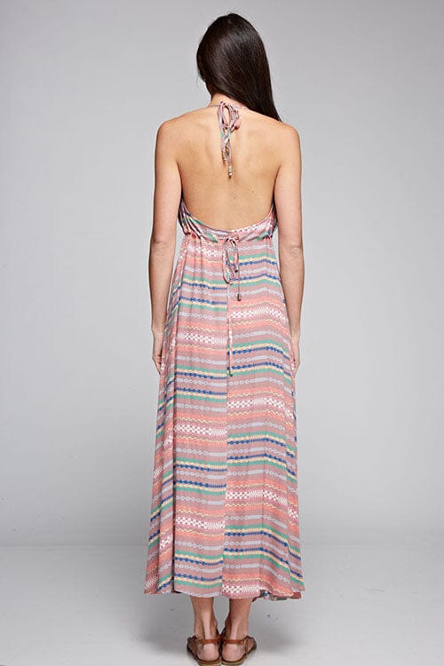 [Color: Brick Multi] A brunette model wearing a boho striped geo print halter maxi dress with a flowy shark bite skirt, open back, and a flattering v-neckline. 