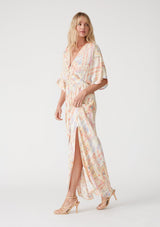 [Color: Butter/Coral] A side facing image of a blonde model wearing a best selling bohemian resort maxi dress in a yellow bohemian diamond print. With half length kimono sleeves, a deep v neckline in the front and back, a back tie closure, a smocked elastic waist, side slits, and a long flowy skirt. 