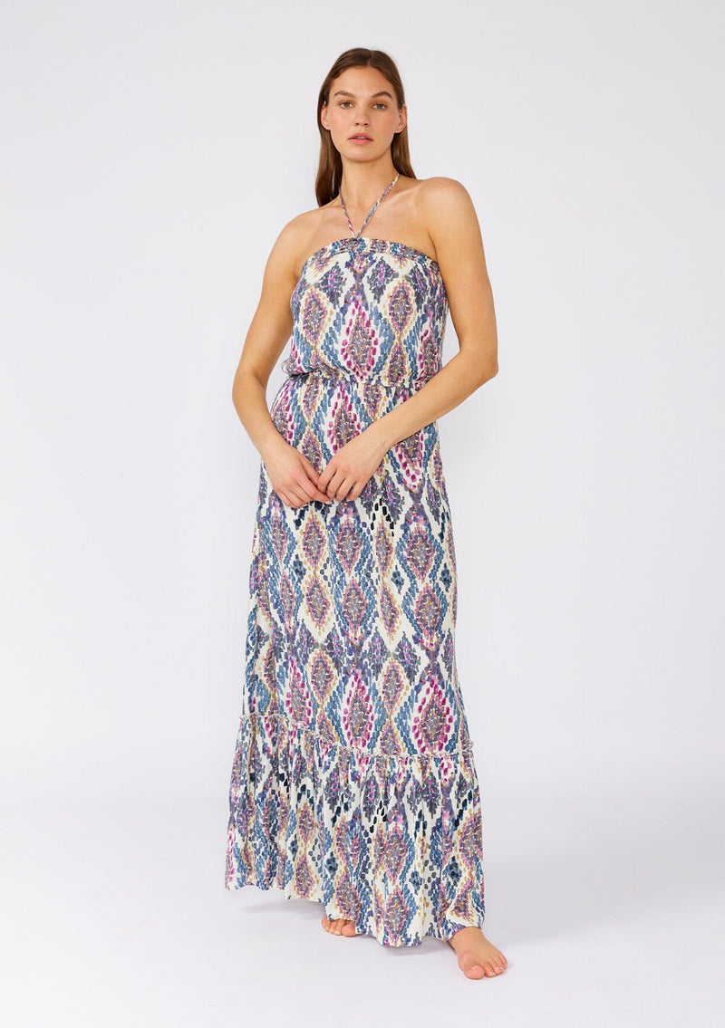 [Color: Natural/Dusty Blue] A front facing image of a brunette model wearing a stunning sleeveless beach maxi dress designed in a blue bohemian print. With a halter neckline and adjustable tie at the back neckline, an elastic waist, and a long flowy skirt with a ruffle trimmed tiered hemline. 