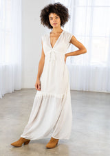 [Color: Off White] A front facing image of a brunette woman wearing a white clip dot chiffon maxi dress with a sleeveless design, a v neckline, and a tie front detail. 