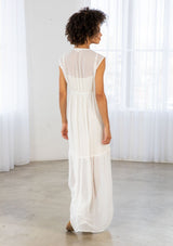 [Color: Off White] A back facing image of a brunette woman wearing a white clip dot chiffon maxi dress with a sleeveless design, a v neckline, and a tie front detail. 