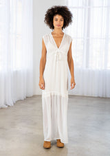 [Color: Off White] A front facing image of a brunette woman wearing a white clip dot chiffon maxi dress with a sleeveless design, a v neckline, and a tie front detail. 